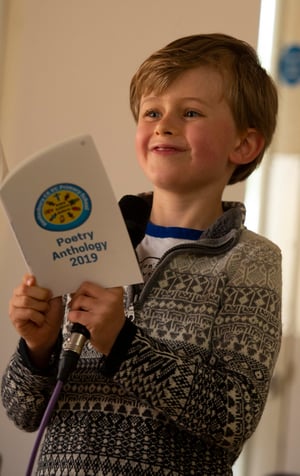 A little boy reads from a self published book of poetry written by his classmates.